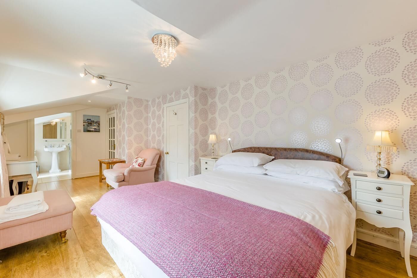 Ein Schlafzimmer mit einem großen Bett, einem Nachttisch mit Lampe, einem Sessel, einer Kommode und einem Spiegel.