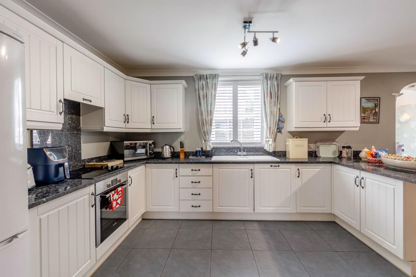 A kitchen with white cabinets, a granite countertop, a built-in oven, and a window with curtains.