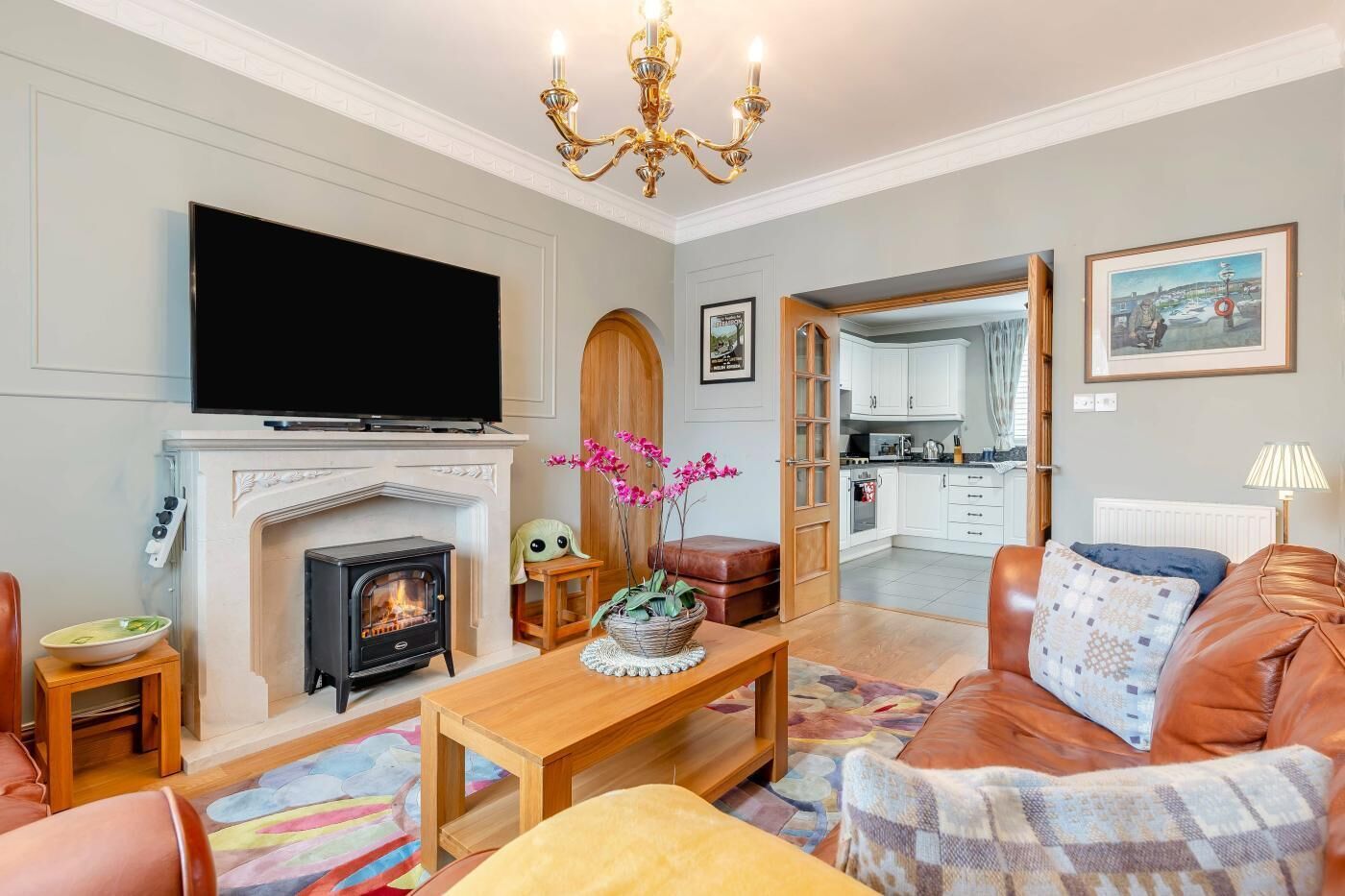 A living room with a fireplace, television, sofa, and a kitchen in the background.