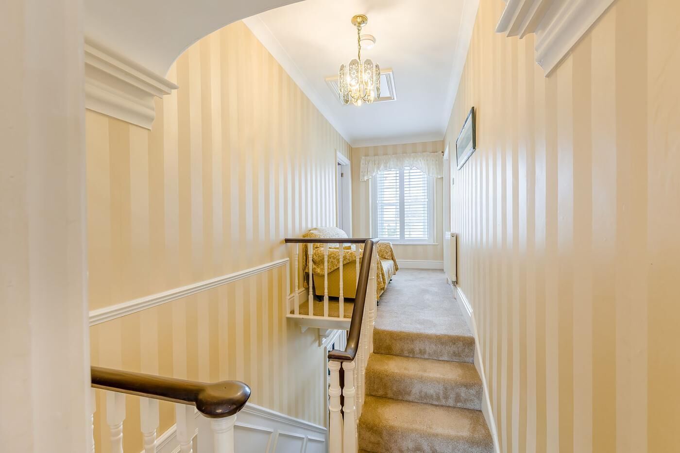 A staircase with a handrail, carpeted steps, and a chandelier.