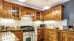 A kitchen with wooden cabinets, a stove, a microwave, and a toaster. - 3 Bed in Tenby (oc-86625) (Tenby)