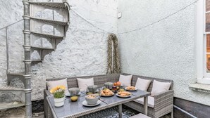 A corner seating area with a table set for breakfast, a wicker sofa, and a decorative metal staircase. - 3 Bed in Tenby (oc-86625) (Tenby)