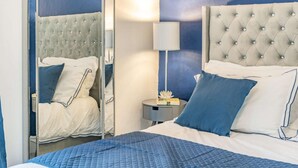 A bedroom with a bed, a nightstand, a mirror, and a lamp. - 3 Bed in Tenby (oc-86625) (Tenby)