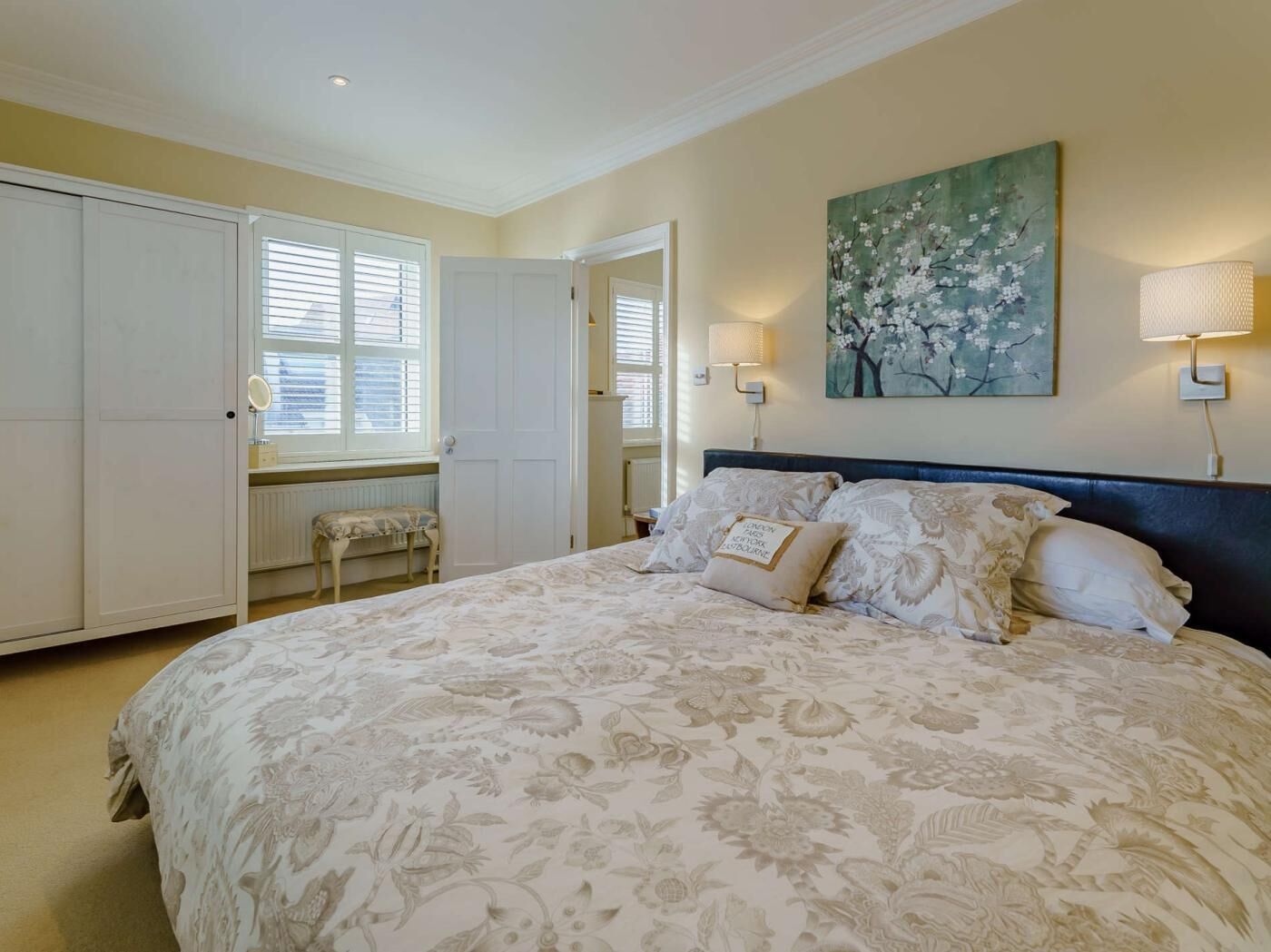 A bedroom with a bed, a nightstand, a lamp, a painting, and a wardrobe.