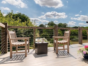 A wooden deck with two chairs and a table, surrounded by a wooden fence and greenery. - 1 Bed in Ipswich (oc-86650) (Aldham)