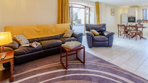 A living room with a sofa, armchair, coffee table, and a dining area with chairs and a table. - 2 Bed in Lampeter (oc-86507) (Cellan)