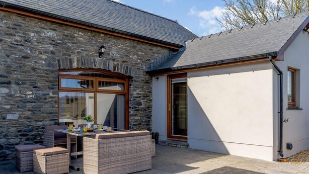 A stone building with a patio area featuring wicker furniture and a table. - 2 Bed in Lampeter (oc-86507) (Cellan)