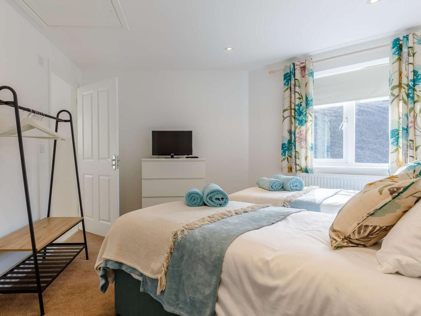 A bedroom with a bed, a TV on a stand, a window with curtains, and a wardrobe.