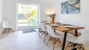 A dining area with a wooden table, white chairs, a vase with flowers, and a painting on the wall. - 3 Bed in Bude (oc-86665) (Bude)