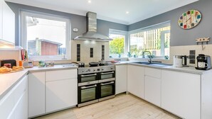 A modern kitchen with white cabinets, a stainless steel range hood, a built-in oven, and a window providing natural light. - 3 Bed in Bude (oc-86665) (Bude)