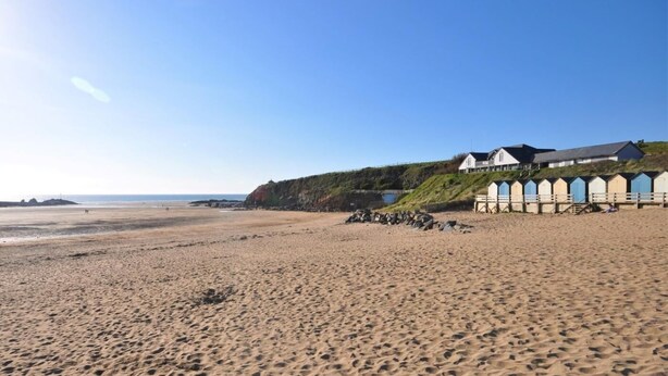 A beach with a row of beach huts and a building on a grassy hill. - 3 Bed in Bude (oc-86665) (Bude)
