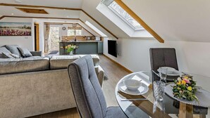 Ein Loft-Wohnzimmer mit Essbereich, einer dahinterliegenden Küche und einem Oberlicht.
