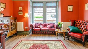 A room with a red sofa, a red armchair, a wooden cabinet, and a patterned rug. - 3 Bed in Broadstairs (oc-86736) (Broadstairs)