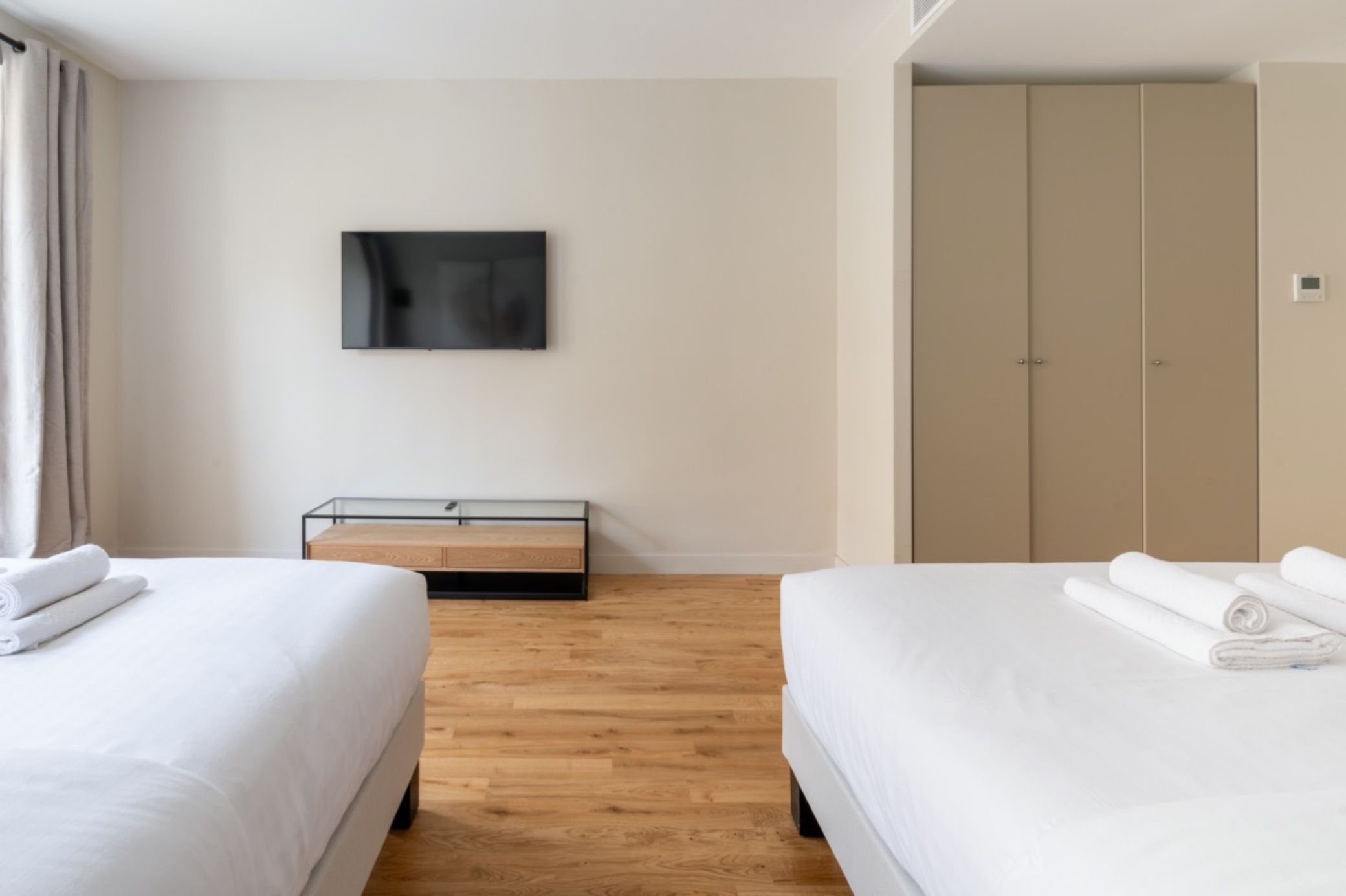 Et hotelværelse med to senge, et fladskærms-tv ophængt på væggen, trægulv og et klædeskab.