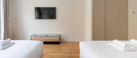 Une chambre d’hôtel avec deux lits, un téléviseur à écran plat fixé au mur, un plancher en bois et une armoire.