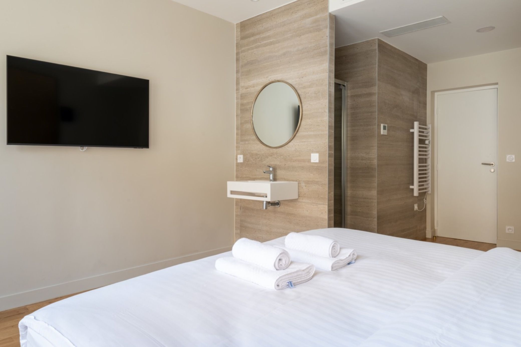 A hotel room with a bed, a TV, a sink, and a mirror.