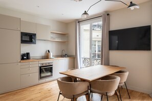 A modern kitchen with a dining area, built-in microwave, oven, and a TV mounted on the wall. - Luxe, State of the Art Suite near Montmartre (Paris)