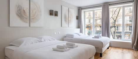 Ein Hotelzimmer mit zwei Betten, einem großen Fenster mit Vorhängen und Bildern an den Wänden.