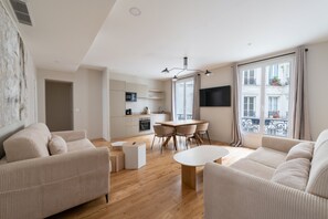 Ein modernes Wohnzimmer mit einer Sofagarnitur, einem Esstisch mit Stühlen und einer Küchenzeile inklusive Schränken und Geräten.