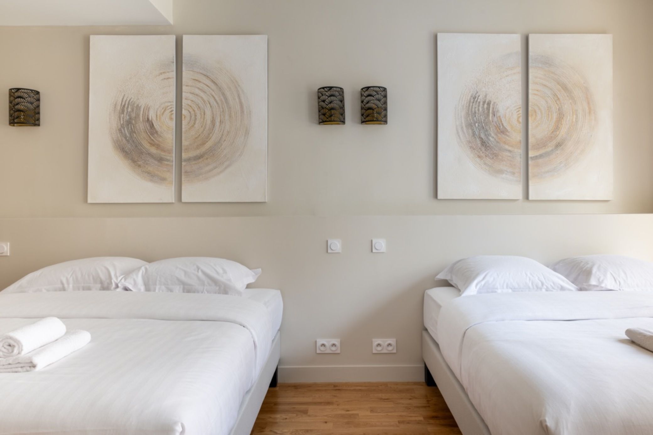 A hotel room with two beds, white bedding, and abstract wall art.