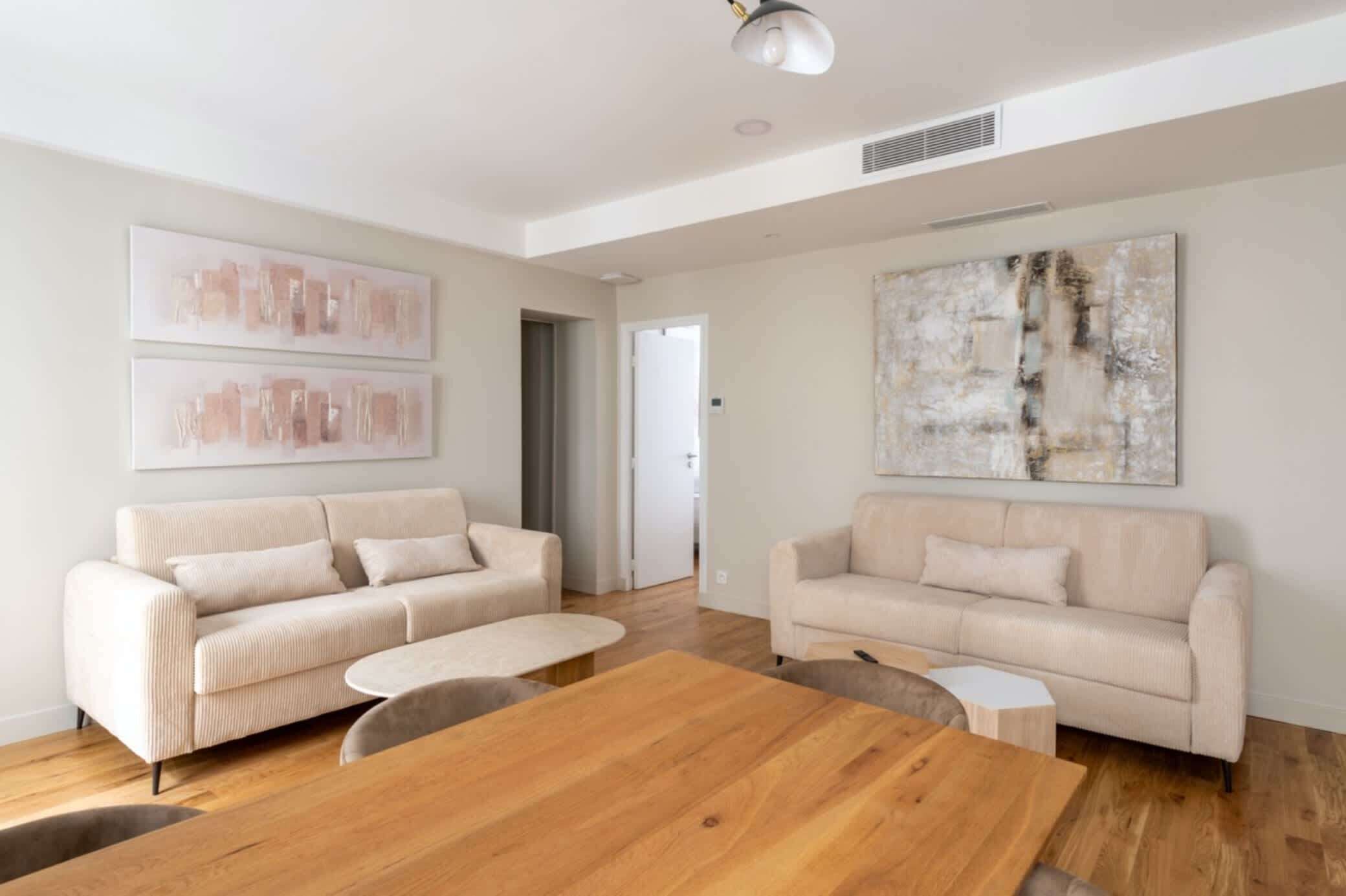 Ein geräumiges Wohnzimmer mit zwei beigen Sofas, einem Holztisch und abstrakter Wandkunst.