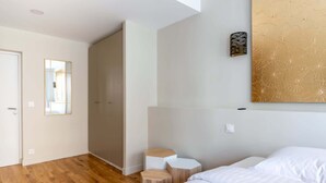 Hotellihuone, jossa on puulattia, sänky, pieni oleskelualue ja seinään kiinnitetty valaisin.