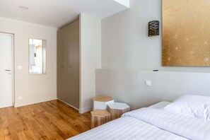 A hotel room with a wooden floor, a bed, a small seating area, and a wall-mounted light fixture. - Luxe, State of the Art Suite near Montmartre (Paris)