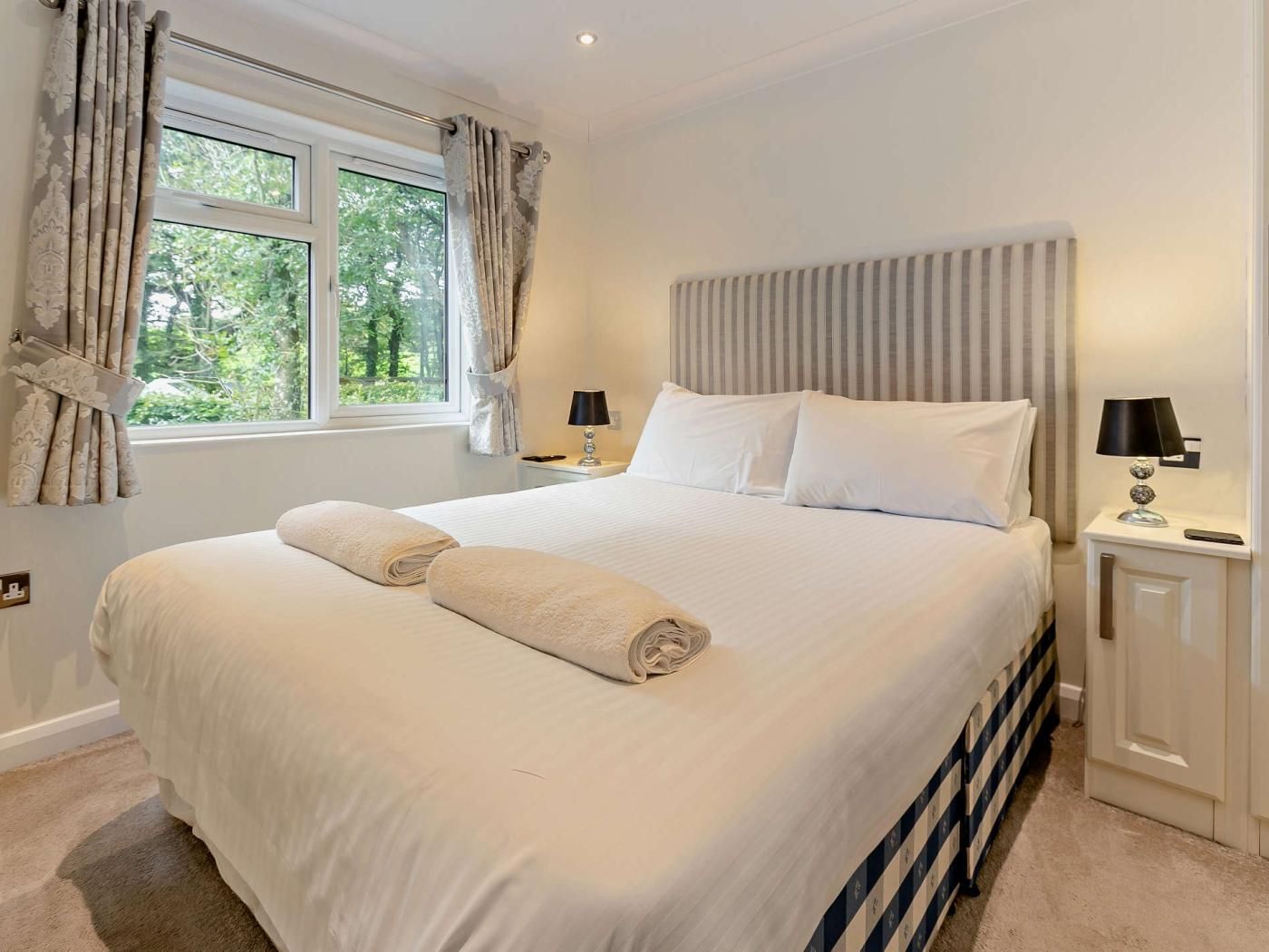 Une chambre d’hôtel avec un grand lit, deux tables de chevet, une fenêtre avec des rideaux et un radiateur.