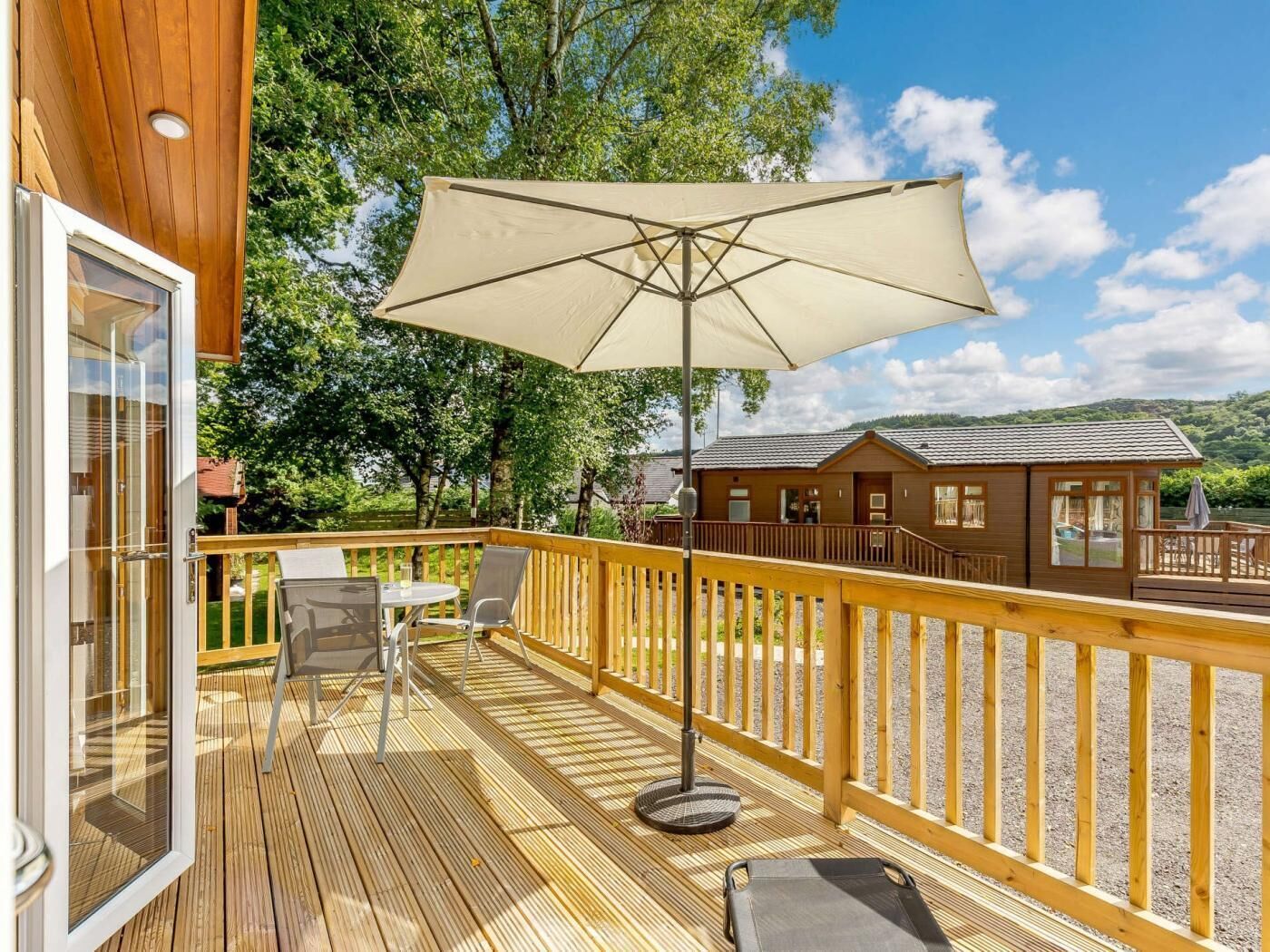 Une terrasse en bois avec une table et des chaises, un grand parasol et un petit bâtiment en arrière-plan.