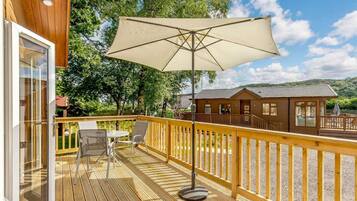 Une terrasse en bois avec une table et des chaises, un grand parasol et un petit bâtiment en arrière-plan.
