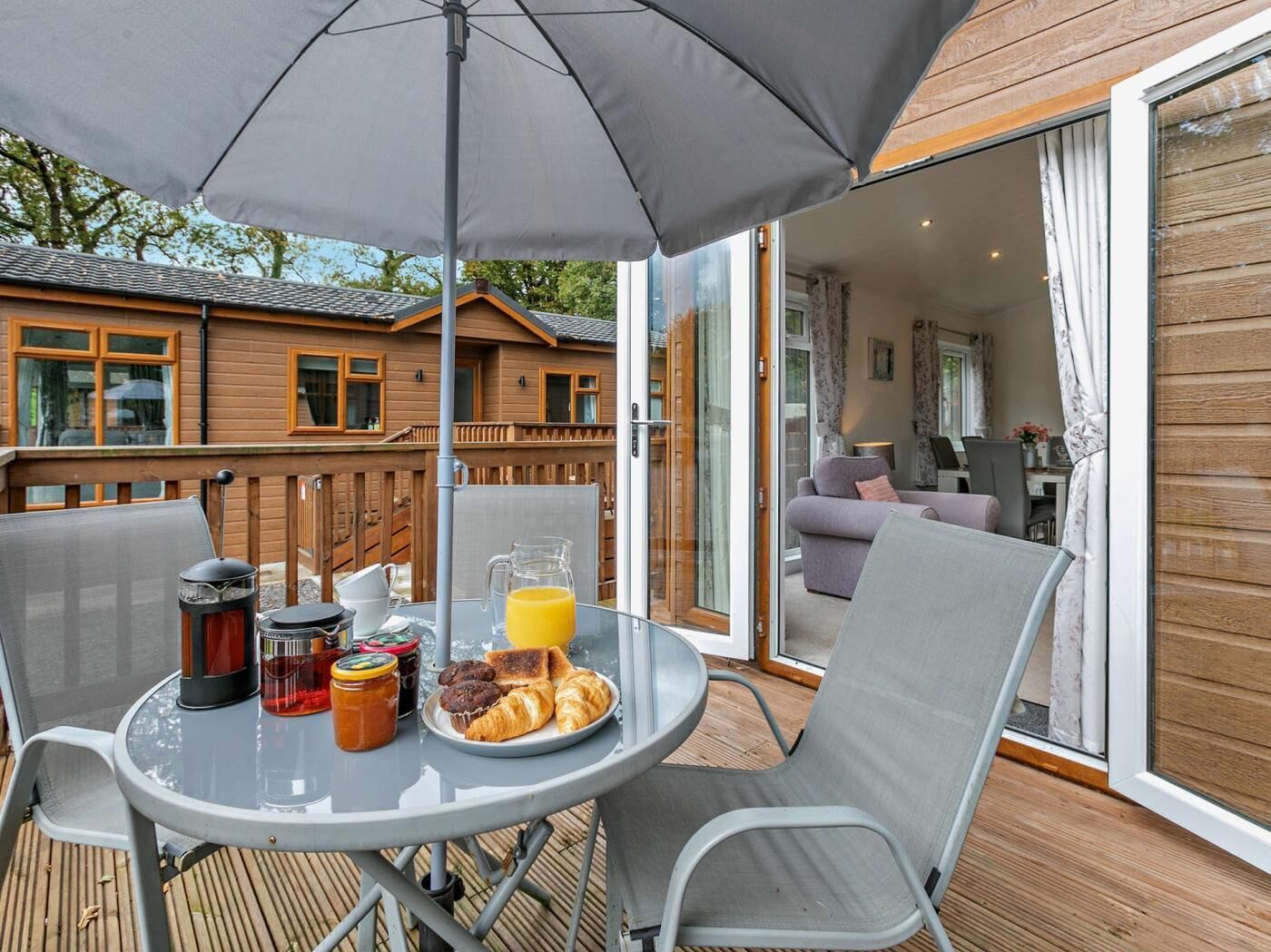 Une terrasse avec une table mise pour le petit-déjeuner, comprenant une carafe de jus d’orange, des croissants et une cafetière.