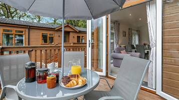 Une terrasse avec une table mise pour le petit-déjeuner, comprenant une carafe de jus d’orange, des croissants et une cafetière.