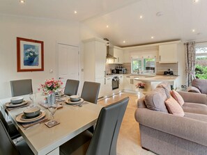 Une cuisine moderne avec des meubles blancs, un coin repas avec une table dressée pour quatre personnes et un salon avec un canapé.
