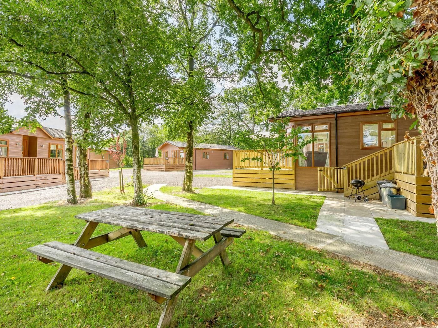 A campsite with wooden cabins, picnic tables, and a barbecue area.