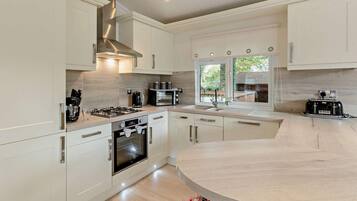 Une cuisine moderne avec des meubles blancs, un four encastré, une cuisinière à gaz, une machine à café et un grille-pain.