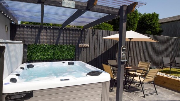 Kylpytynnyri, jonka yläpuolella on pergola, ulkona oleva oleskelualue ja kyltti, joka kertoo, että kylpytynnyri lämpiää oluella.