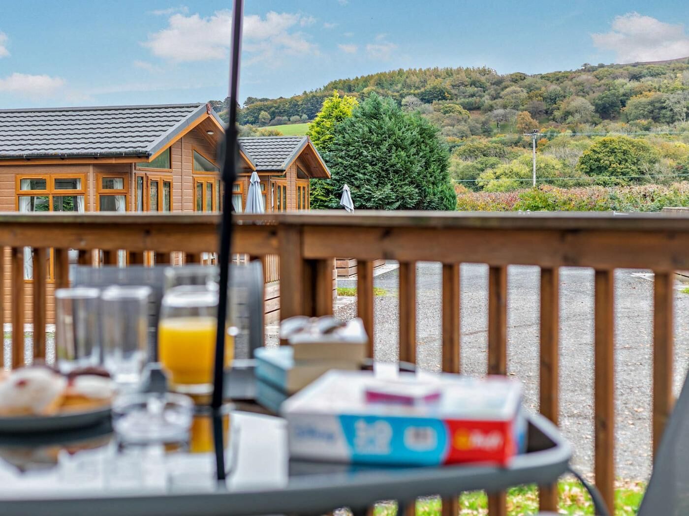 Une terrasse en bois avec des éléments pour le petit-déjeuner et une vue sur un chalet doté d’un toit en tuiles.