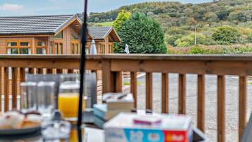 Une terrasse en bois avec des éléments pour le petit-déjeuner et une vue sur un chalet doté d’un toit en tuiles.