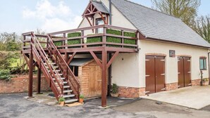 A building with a staircase leading to a balcony, a garage door, and a small garden area. - 1 Bed in Hawarden (oc-86711) (Dobshill)