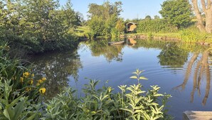 A calm river with lush greenery and a wooden structure in the distance. - 1 Bed in Hawarden (oc-86711) (Dobshill)