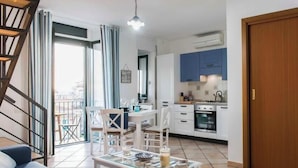 A modern living room with a sofa, coffee table, and dining area. A kitchen with cabinets and appliances is visible in the background. - Palazzo Carrano (Vietri sul Mare)