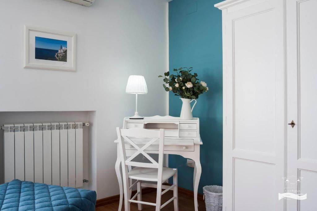 A bedroom with a bed, a desk with a lamp, a vase with flowers, and a radiator.