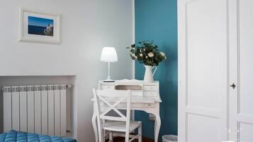 A bedroom with a bed, a desk with a lamp, a vase with flowers, and a radiator.