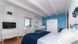 A bedroom with a bed, a TV on a dresser, a desk, and a view of the outdoors. - Palazzo Carrano (Vietri sul Mare)