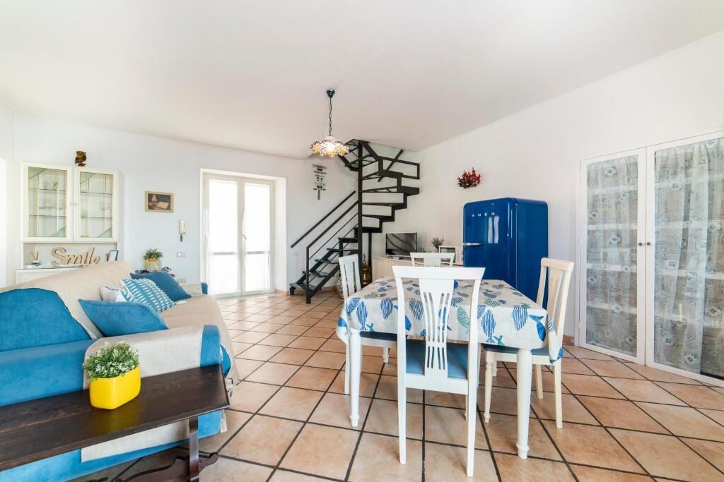 Uma sala de estar com sofá, mesa de jantar, cadeiras, escada e cozinha.