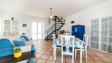 Uma sala de estar com sofá, mesa de jantar, cadeiras, escada e cozinha.