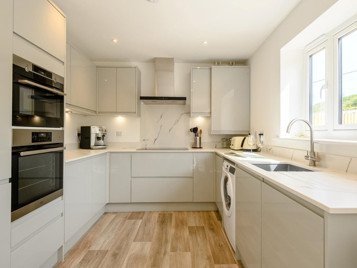 A modern kitchen with built-in appliances, a washing machine, and a window providing natural light.