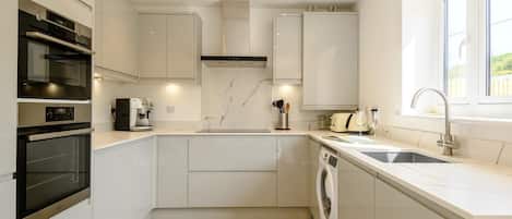 A modern kitchen with built-in appliances, a washing machine, and a window providing natural light.