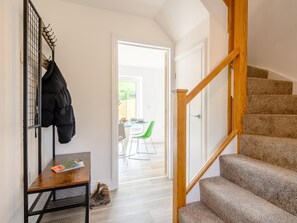 Eine Treppe mit hölzernen Geländern, ein Kleiderständer mit einer Jacke und ein Tisch mit einer Zeitschrift und einem Schuhpaar.