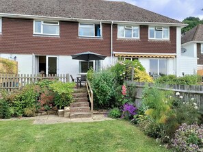 Ein zweistöckiges Haus mit Garten, Holzzaun und einer Terrasse mit Tisch und Stühlen.